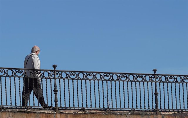 Persona mayor protegido con mascarilla pasea por el puente de Triana.